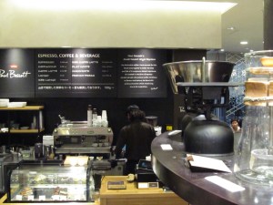 Coffee Items on a Shelf in foreground Barista on espresso machine in background at Paul Bassett Coffee Shibuya Tokyo Japan